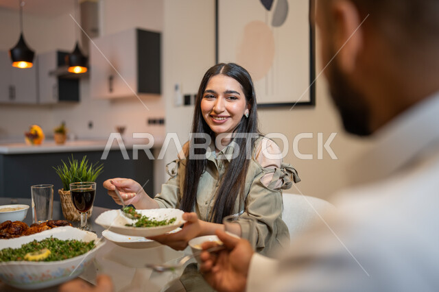 تناول وجبة الغداء، ايماءات وتعابير تدل على السعادة, أجواء عائلية سعيدة, زوجان عربيان خليجيان سعوديان يجلسان على مائدة الطعام المليئة بأصناف متنوعة وشهية, قضاء أوقات ممتعة مع العائلة