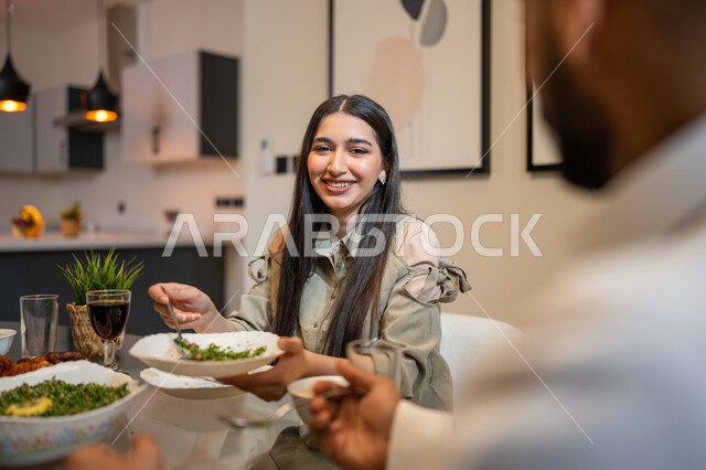 تعابير و ايماءات تدل على السعادة, تناول وجبة الغداء، أجواء عائلية سعيدة, زوجان عربيان خليجيان سعوديان يجلسان على مائدة الطعام المليئة بأصناف متنوعة وشهية, قضاء أوقات ممتعة مع العائلة