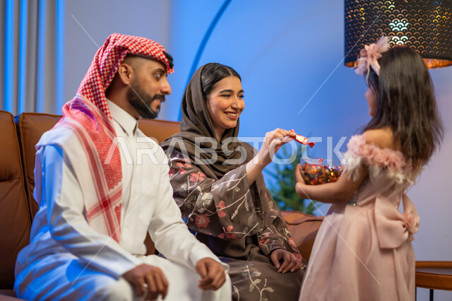 أجواء العيد في المجتمع العربي السعودي, فتاة عربية خليجية سعودية تقوم بتقديم قطع الشوكولاتة في مناسبة العيد السعيد, تجمع أسري لعائلة عربية خليجية سعودية في غرفة الجلوس ,حسن استقبال واكرام الضيوف, مناسبات و أعياد إسلامية