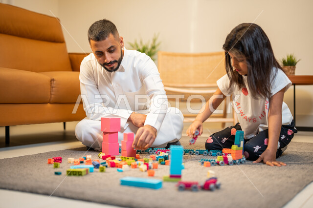 الاستمتاع واللعب بالمكعبات، اب عربي خليجي سعودي يشارك ابنته اللعب، انشطة ترفيهية للابناء، الجلوس في غرفة المعيشة، رعاية وتشجيع و تطوير مهارات الأطفال، الاهتمام ودعم الأبناء، قضاء اوقات عائلية ممتعة
