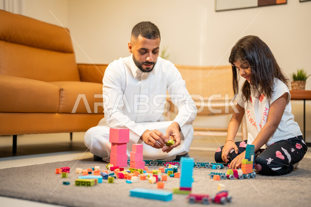 الاستمتاع واللعب بالمكعبات، اب عربي خليجي سعودي يشارك ابنته اللعب، انشطة ترفيهية للابناء، الجلوس في غرفة المعيشة، رعاية وتشجيع و تطوير مهارات الأطفال، الاهتمام ودعم الأبناء، قضاء اوقات عائلية ممتعة