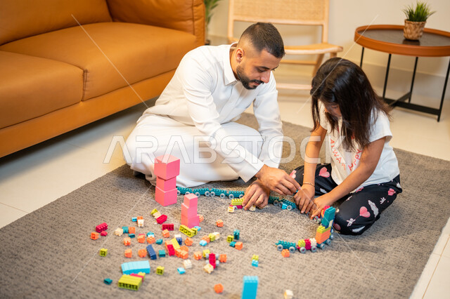 رعاية وتشجيع و تطوير مهارات الأطفال، اب عربي خليجي سعودي يشارك ابنته اللعب، انشطة ترفيهية للابناء، الاستمتاع واللعب بالمكعبات، الجلوس في غرفة المعيشة، الاهتمام ودعم الأبناء، قضاء اوقات عائلية ممتعة