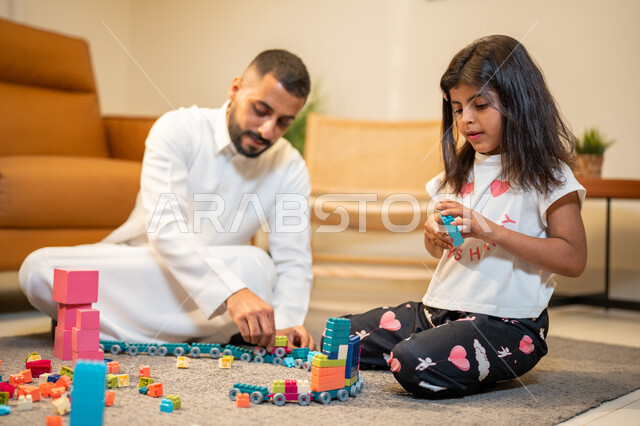قضاء اوقات عائلية ممتعة، اب عربي خليجي سعودي يشارك ابنته اللعب، انشطة ترفيهية للابناء، الاستمتاع واللعب بالمكعبات، الجلوس في غرفة المعيشة، رعاية وتشجيع و تطوير مهارات الأطفال، الاهتمام ودعم الأبناء
