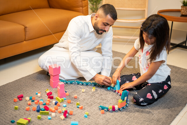 قضاء اوقات عائلية ممتعة، اب عربي خليجي سعودي يشارك ابنته اللعب، انشطة ترفيهية للابناء، الاستمتاع واللعب بالمكعبات، الجلوس في غرفة المعيشة، رعاية وتشجيع و تطوير مهارات الأطفال، الاهتمام ودعم الأبناء