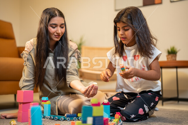 الاستمتاع بتركيب المكعبات، ام عربية خليجية سعودية تلعب مع ابنتها، ايماءات وجه تدل على السعادة، مفهوم الأمومة والطفولة، رعاية وتشجيع وتطوير مهارات الأطفال، الاهتمام بالأبناء ودعمهم، قضاء اوقات عائلية ممتعة