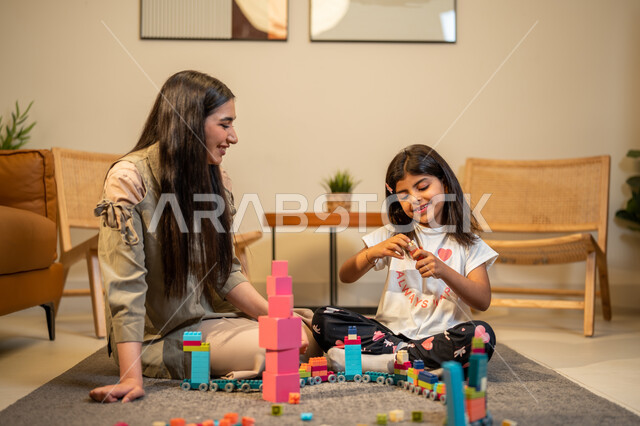 الاهتمام بالأبناء ودعمهم، ام عربية خليجية سعودية تلعب مع ابنتها، الاستمتاع بتركيب المكعبات، ايماءات وجه تدل على السعادة، مفهوم الأمومة والطفولة، رعاية وتشجيع وتطوير مهارات الأطفال، قضاء اوقات عائلية ممتعة