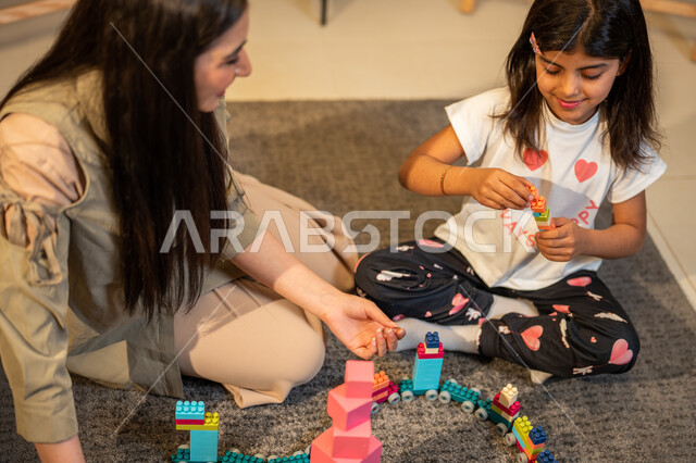 الاهتمام بالأبناء ودعمهم، ام عربية خليجية سعودية تلعب مع ابنتها، الاستمتاع بتركيب المكعبات، ايماءات وجه تدل على السعادة، مفهوم الأمومة والطفولة، رعاية وتشجيع وتطوير مهارات الأطفال، قضاء اوقات عائلية ممتعة