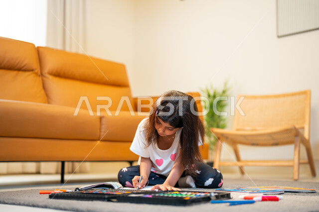 Coloring tools and equipment, learning, creativity and skills development, a Saudi Arabian Gulf girl sitting in the living room and creating creativity by coloring pictures, spending fun times, drawing coloring game, facial gestures indicating happiness, 
