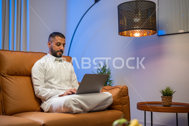 عقد إجتماع عمل عبر الإنترنت، إستخدام جهاز الحاسوب المحمول، رجل عربي خليجي سعودي يجلس في غرفة المعيشة ،التسويق لموقع إلكتروني، إجراء مكالمة فيديو، مشاهدة الأفلام والمسلسلات