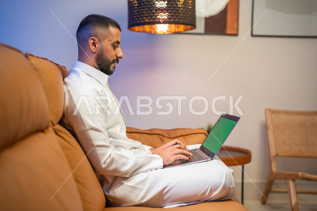 إجراء مكالمة فيديو، استخدام جهاز الحاسوب المحمول بخلفية خضراء كروما، رجل عربي خليجي سعودي يجلس في غرفة المعيشة ، التسويق لموقع إلكتروني، مشاهدة الأفلام والمسلسلات