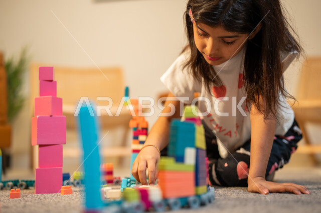 قضاء اوقات ممتعة، طفلة عربية خليجية سعودية تستمتع بتركيب المكعبات، الجلوس في غرفة المعيشة، ايماءات وجه تدل على السعادة، الابداع وتنمية المهارات، انشطة ترفيهية ابداعية
