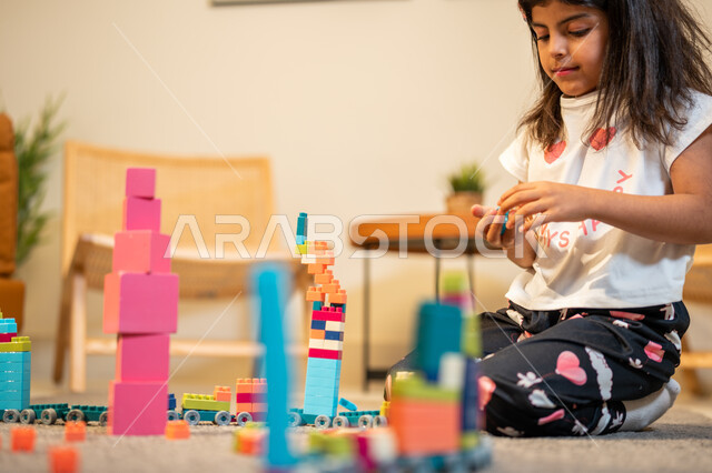 قضاء اوقات ممتعة، طفلة عربية خليجية سعودية تستمتع بتركيب المكعبات، الجلوس في غرفة المعيشة، ايماءات وجه تدل على السعادة، الابداع وتنمية المهارات، انشطة ترفيهية ابداعية