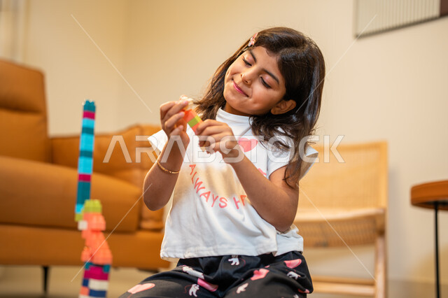 الابداع وتنمية المهارات، طفلة عربية خليجية سعودية تستمتع بتركيب المكعبات، الجلوس في غرفة المعيشة، ايماءات وجه تدل على السعادة، انشطة ترفيهية ابداعية، قضاء اوقات ممتعة