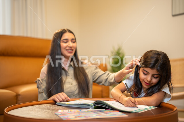 ام عربية سعودية خليجية تقوم بتعليم ابنتها، مساعدة الابناء في تأدية الواجبات المدرسية، الانشطة التعليمية وتنمة القدرات، تعلم وتطوير الابناء، الاهتمام بتعليم بالأبناء ودعمهم