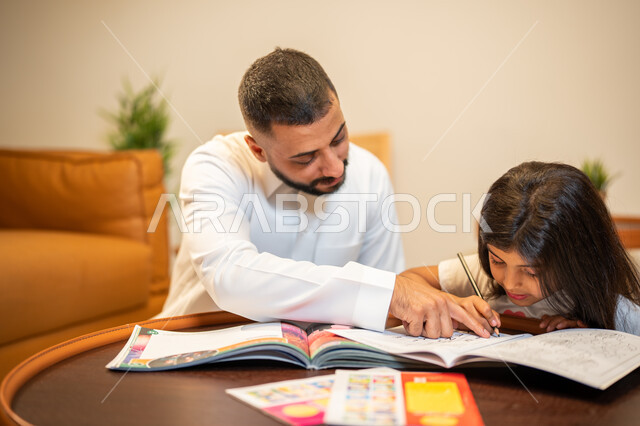 Helping children in performing homework, a Saudi Arabian Gulf father teaching his daughter, educational activities and capacity development, learning and developing children, interest in educating and supporting children