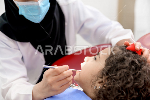 طفلة عربية سعودية خليجية في موعد عند طبيبة الأسنان ، معالجة الاسنان والتسوس ، عيادة أسنان خاصة بالأطفال ، الفحص الطبي للاطفال ، مفهوم الطب والرعاية الصحية