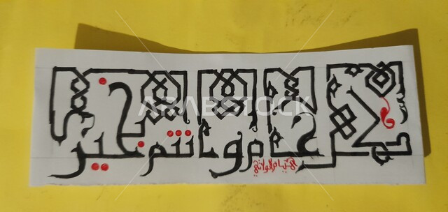 مخطوطة يدوية على ورقة بيضاء بعبارة تهنئة في العيد, كل عام و أنتم بخير, استخدام الخط الكوفي في الكتابة, خلفية صفراء.