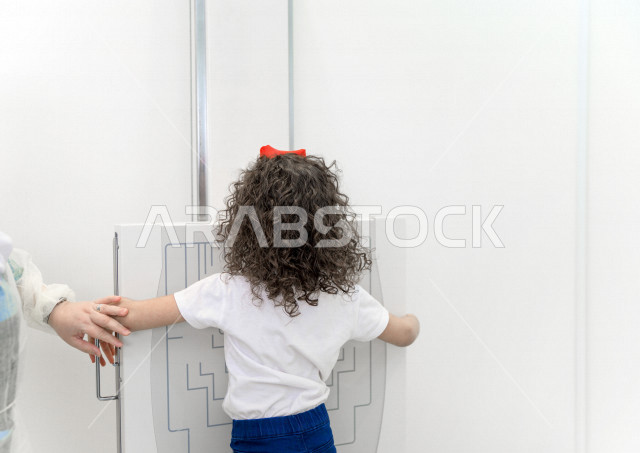 A Saudi Arabian girl stands correctly on a specialized x-ray machine for teeth, dental examination and treatment, a pediatric dental clinic, medical and healthcare concept