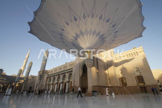 The courtyard of the Prophet's Mosque in Medina, Saudi Arabia, worship and closeness to God, the Noble Prophet's Mosque, Islamic holy places, Muslims walking in the outer complex of the Prophet's Mosque in Medina, electronic umbrellas