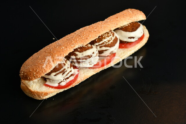 Light Arabic breakfast, sandwich with falafel discs and tahini sauce with fresh tomato slices, fast food restaurants, black background.