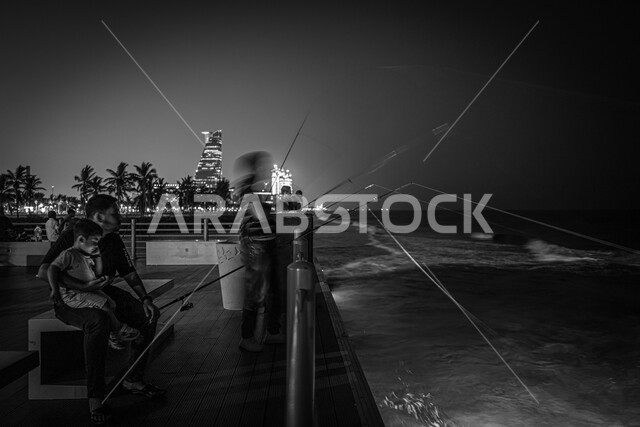 الواجهة البحرية لكورنيش مدينة جدة في المملكة العربية السعودية ليلا، صورة بالأبيض والأسود لأب مع ابنه يتأمل جمال وهدوء البحر، الابراج وناطحات السحاب، معالم جدة السياحية المشهورة.
