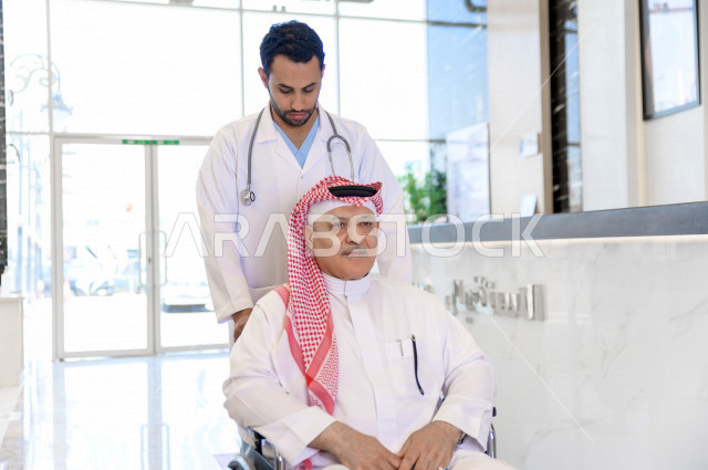 طبيب سعودي خليجي يشرف على علاج رجل مسن مريض على كرسي متحرك ،ايماءات وجه ويدين مختلفة ،موعد مع الطبيب لتلقي العلاج ، مستشفى خاص بكبار السن ، مفهوم الطب والرعاية الصحية