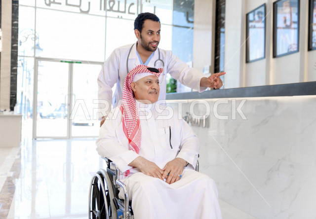 طبيب سعودي خليجي يشرف على علاج رجل مسن مريض على كرسي متحرك ،ايماءات وجه ويدين مختلفة ،موعد مع الطبيب لتلقي العلاج ، مستشفى خاص بكبار السن ، مفهوم الطب والرعاية الصحية