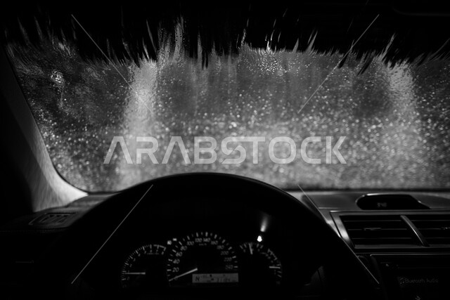 صورة بالأسود و الأبيض لواجهة السيارة من الداخل  أثناء عملية الغسل, تنظيف السيارات عن طريق الغسيل الآلي,  استخدام التقنيات الحديثة لتنظيف و صيانه و تلميع السيارات, مغسل آلي في المملكة العربية السعودية.