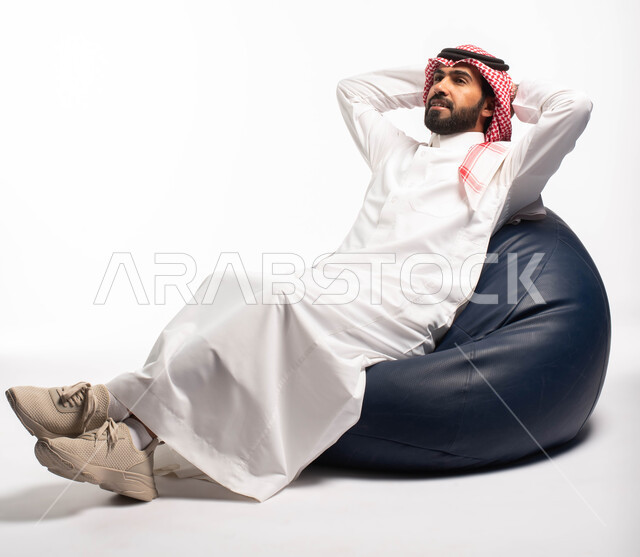 الحاجة إلى النوم، الشعور بالتعب و الخمول , إيماءات يدين تدل على الراحة والإسترخاء ، بورتريه لرجل عربي سعودي خليجي يرتدي الثوب التقليدي يجلس على كرسي طري ومريح , خلفية بيضاء