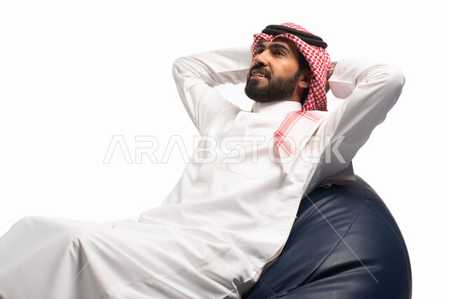 الشعور بالتعب و الخمول , إيماءات يدين تدل على الراحة والإسترخاء ، بورتريه مقرب لرجل عربي سعودي خليجي يرتدي الثوب التقليدي يجلس على كرسي طري ومريح ,  الحاجه الى النوم , خلفية بيضاء