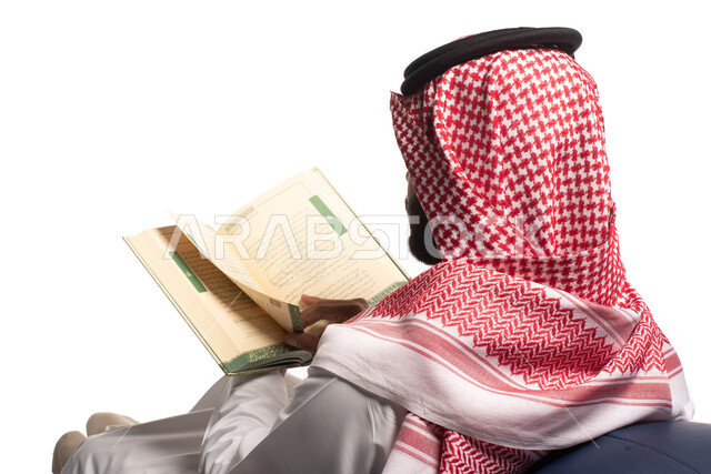 التمعن والتركيز، قضاء الوقت بالقراءة والتعلم والثقافة ، بورتريه مقرب من الخلف لرجل عربي سعودي خليجي يرتدي الزي السعودي التقليدي يجلس على كرسي مريح ويحمل بيديه كتاب، خلفية بيضاء
