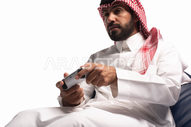 Spending an enjoyable and entertaining time, interacting and merging with PlayStation games, modern entertaining technologies, a portrait of a Saudi Arabian Gulf man dressed in traditional dress, sitting on a comfortable chair, holding a joystick in his h