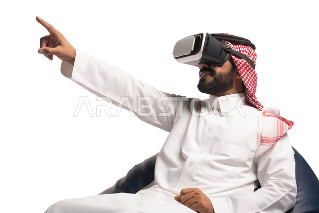 استخدام حاسة اللمس لتحريك العناصر الهولوجرامية، الاستمتاع بمشاهدة أفلام الواقع الافتراضي، بورتريه مقرب لرجل عربي خليجي سعودي يجلس على كرسي مريح ويرتدي نظارة الواقع الافتراضي ثلاثية الابعاد، خلفية بيضاء