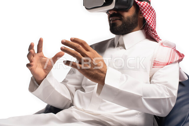 قضاء أوقات ممتعة ومسلية بالألعاب الافتراضية، الاستمتاع بمشاهدة أفلام الواقع الافتراضي، بورتريه مقرب لرجل عربي خليجي سعودي يجلس على كرسي مريح ويرتدي نظارة الواقع الافتراضي ثلاثية الابعاد، خلفية بيضاء
