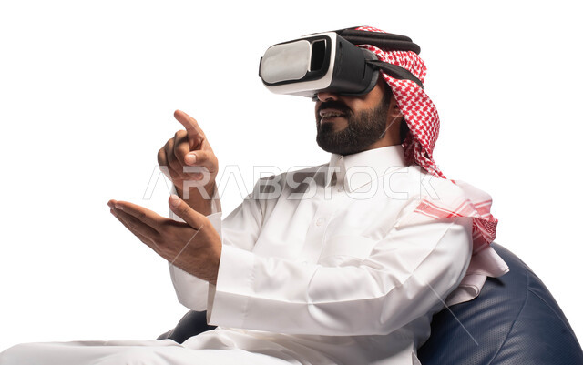 استخدام حاسة اللمس لتحريك العناصر الهولوجرامية، الاستمتاع بمشاهدة أفلام الواقع الافتراضي، بورتريه مقرب لرجل عربي خليجي سعودي يجلس على كرسي مريح ويرتدي نظارة الواقع الافتراضي ثلاثية الابعاد، خلفية بيضاء