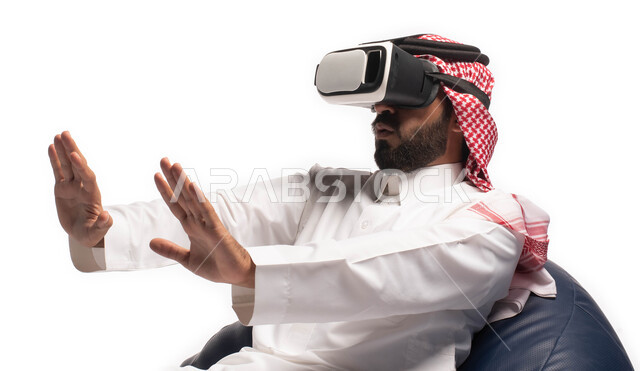 الاستمتاع بمشاهدة أفلام الواقع الافتراضي، استخدام حاسة اللمس لتحريك العناصر الهولوجرامية، بورتريه مقرب لرجل عربي خليجي سعودي يجلس على كرسي مريح ويرتدي نظارة الواقع الافتراضي ثلاثية الابعاد، خلفية بيضاء