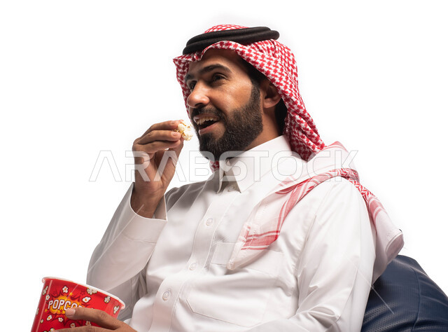 Watching a movie, spending fun and entertaining times, a close-up portrait of a Saudi Arabian Gulf man wearing traditional dress holding a box of popcorn in his hand and enjoying watching movies, face and hand gestures indicating happiness and enjoyment, 