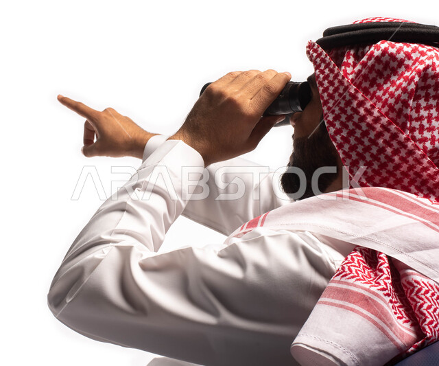 Love of exploration and adventure, seeing distant things through binoculars, a close-up portrait of a Saudi Arabian Gulf man wearing traditional dress sitting on a comfortable chair and looking through the binoculars and pointing with his hand at somethin