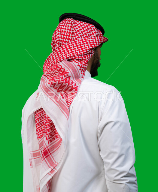 ايماءات جسد تدل على الثقة و القوة, بورتريه من الخلف لشاب عربي سعودي خليجي يرتدي الشماغ و الثوب السعودي التقليدي يقف بإستقامة, الاهتمام بالمظهر الخارجي، كروما، خلفية خضراء.