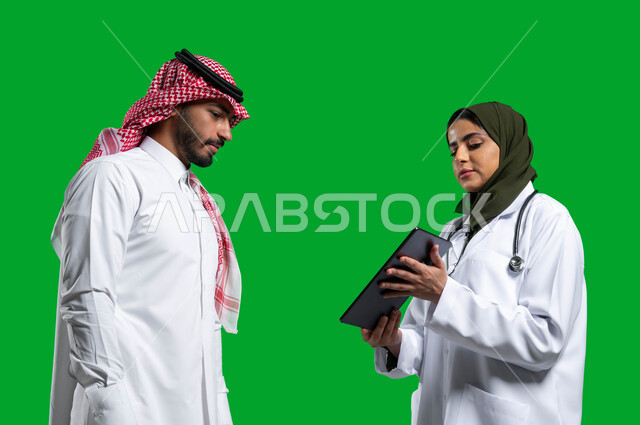 وصف الحالة المرضية وتقديم الاستشارات الطبية، متابعة السجل الطبي الالكتروني الخاص بالمريض, بورتريه مقرب  لطبيبة عربية خليجية سعودية ترتدي المعطف والسماعة الطبية تحمل بيدها التابلت، وصف العلاج لمريض سعودي يرتدي الزي التقليدي، مهن نسائية، كروما، خلفية خضراء.