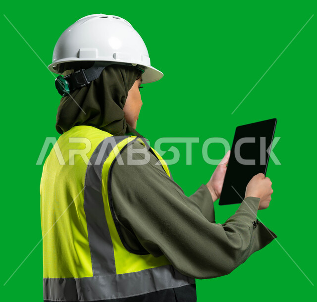 عرض المخططات و التصماميم الهندسية الالكترونية على جهاز التابلت, بورتريه جانبي مقرب لمهندسة معمارية عربية خليجية سعودية ترتدي الخوذة وسترة الحماية، مهن ووظائف نسائيه، مفهوم الهندسة و الإنشاءات المعمارية, رؤية2030, كروما، خلفية خضراء.