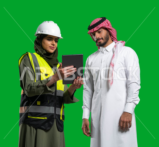 مهن ووظائف نسائيه، عرض التصاميم المعماريه و المخططات الهندسية الإلكترونية على جهاز التابلت, بورتريه لمهندسة معمارية عربية خليجية سعودية ترتدي الخوذة وسترة الحماية تتحدث مع رجل عربي خليجي سعودي يرتدي الزي التقليدي, رؤية 2030, كروما، خلفية خضراء.