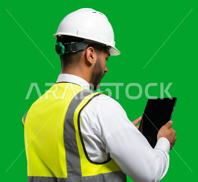 Electronic engineering drawings and designs, merging work with technology and technology, a close-up portrait of a Saudi Arabian Gulf engineer wearing a helmet and a protection jacket holding a tablet in his hand, the concept of engineering and architectu