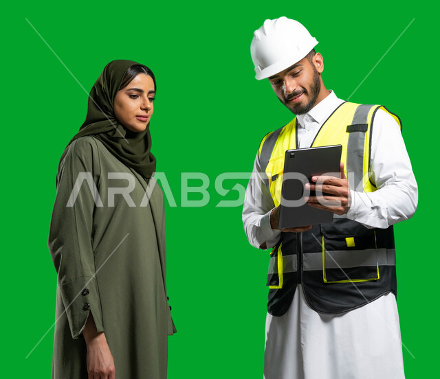 The concept of construction and architecture, integrating work with technology and technology, electronic engineering plans and designs, a portrait of a Saudi Arabian Gulf engineer wearing a helmet and protection jacket holding a tablet in his hand and ta