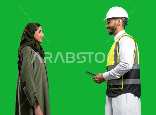 Merging work with technology and technology, electronic engineering plans and designs, a portrait of a Saudi Arab Gulf engineer wearing a helmet and a protection jacket holding a tablet in his hand and talking with a veiled Saudi Gulf Arab woman, the conc
