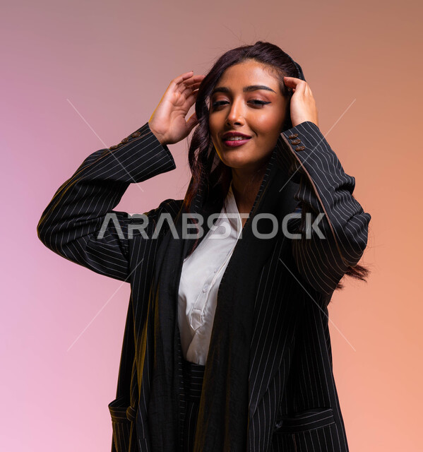 الاهتمام بالمظهر الخارجي و الاناقة بمتابعة صيحات الموضة والجمال، بورتريه مقرب لإمرأة عربية خليجية سعودية ترتدي لباس رسمي عصري حديث تقوم بتصفيف وترتيب شعرها، ملابس نسائية بتصاميم عصرية، خلفية ملونة