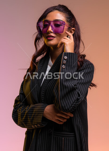 ملابس نسائية بتصاميم عصرية، متابعة الموضة والجمال والاناقة، بورتريه مقرب لإمرأة عربية خليجية سعودية ترتدي لباس رسمي عصري حديث ونظارات شمسية تضع يدها على خدها، تسوق وشراء أحدث المنتجات السعودية والعالمية الفاخرة، خلفية ملونة