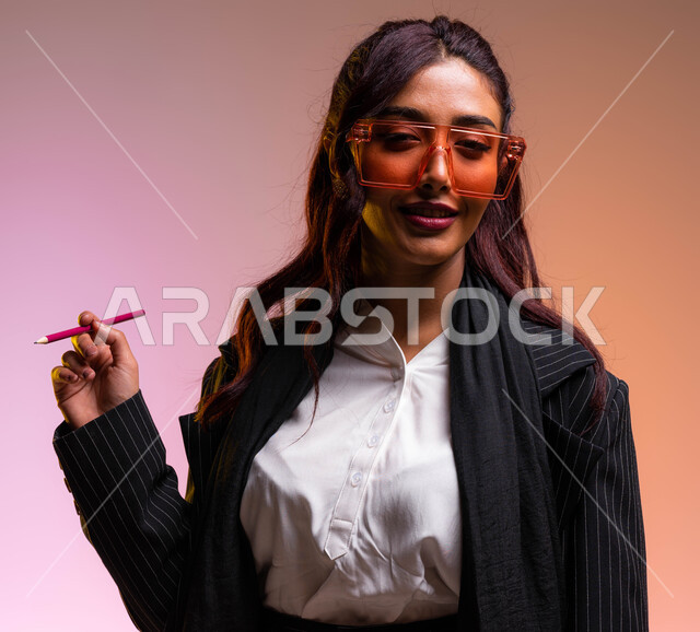 استاذة أنيقة ترتدي نظارات شمسية ملونة عصرية، أعمال ومهن نسائية سعوديه، بورتريه مقرب  لسيدة اعمال عربية خليجية سعودية مبتسمة ترتدي اللباس الرسمي تمسك بيدها قلم تنظر الى الكاميرا, الاهتمام والاعتناء بالمظهر الخارجي والاناقه، خلفية ملونة