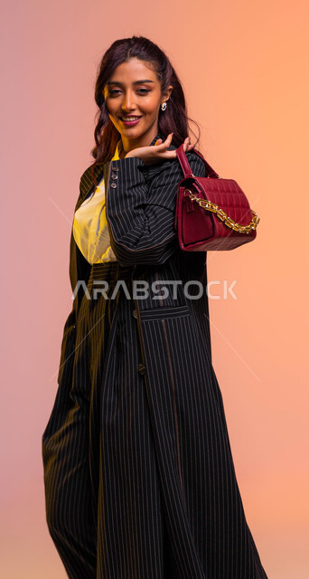 مواكبة تصاميم الأزياء والموديلات الحديثة, بورتريه لعارضة عربية خليجية سعودية  مبتسمة ترتدي لباس رسمي عصري حديث وتحمل بيدها حقيبة جلديه بايماءات الأنوثة واللطافة, التسويق للمنتجات السعودية والماركات العالمية الفاخرة, خلفية ملونة