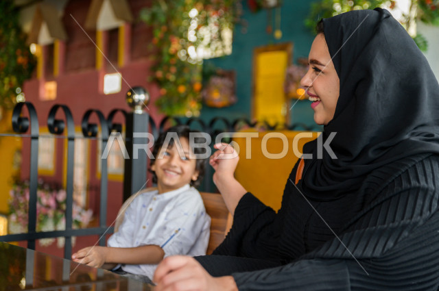 طفل عربي خليجي سعودي يقضي وقته مع والدته في المطعم بايماءات و تعابير وجه تدل على السعادة ، قضاء العطلة مع العائلة ، أجواء عائلية ترفيهية ، جلسات فريدة و مميزة ، مطاعم و كافيهات في السعودية